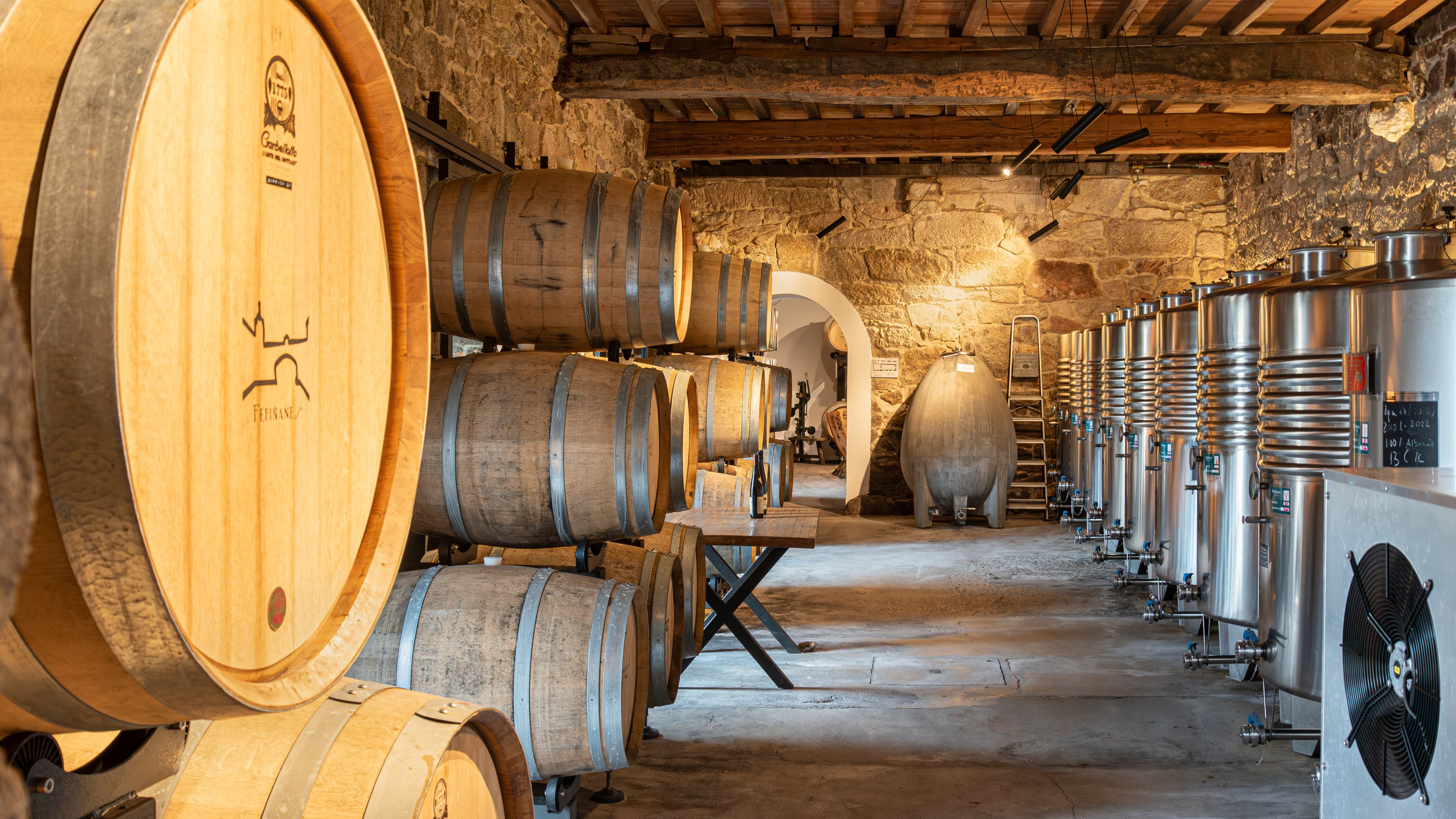 Barrels and modern winery equipment inside a stone cellar at Palacio de Fefiñanes
